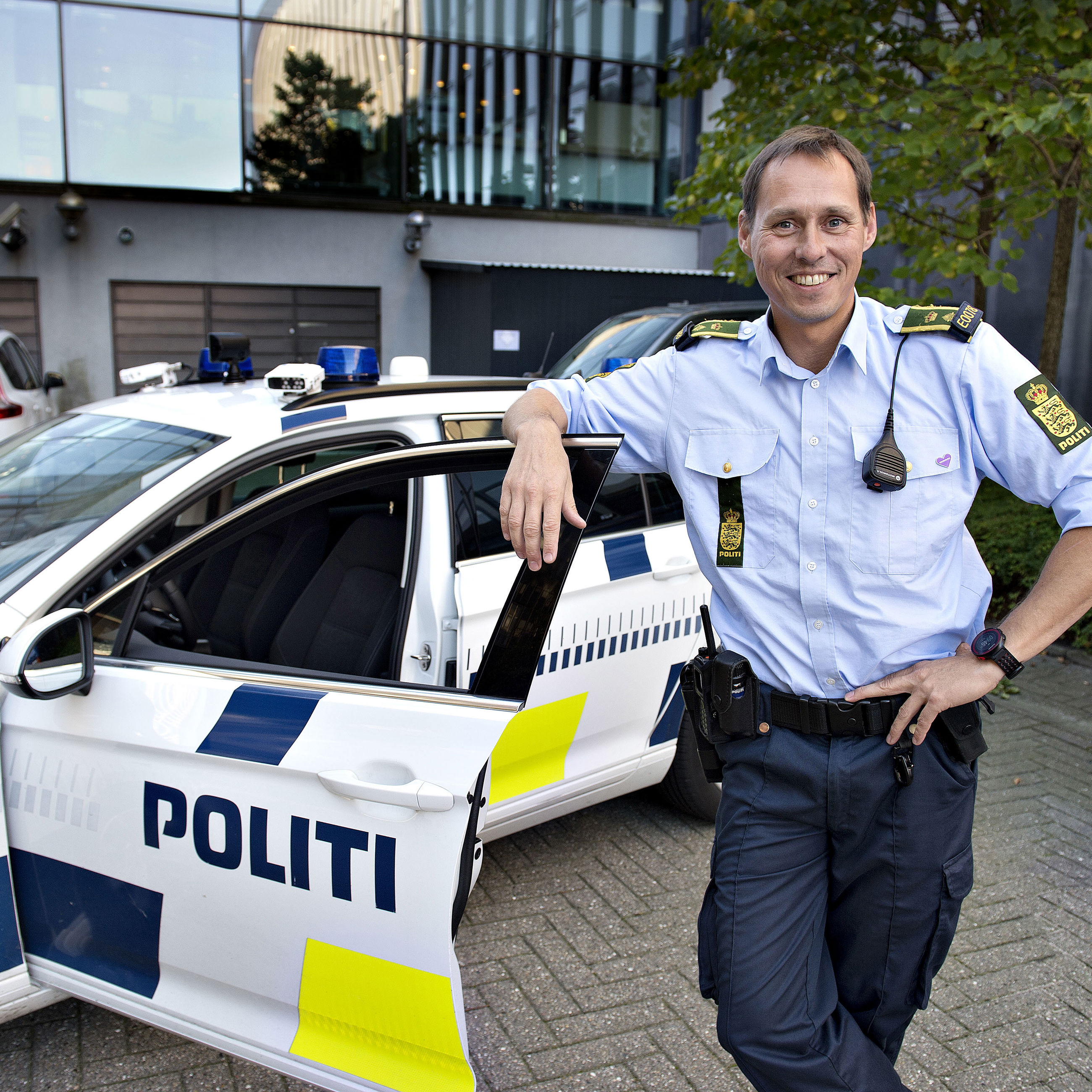 Politibetjent, der læner sig op af døren til politibil