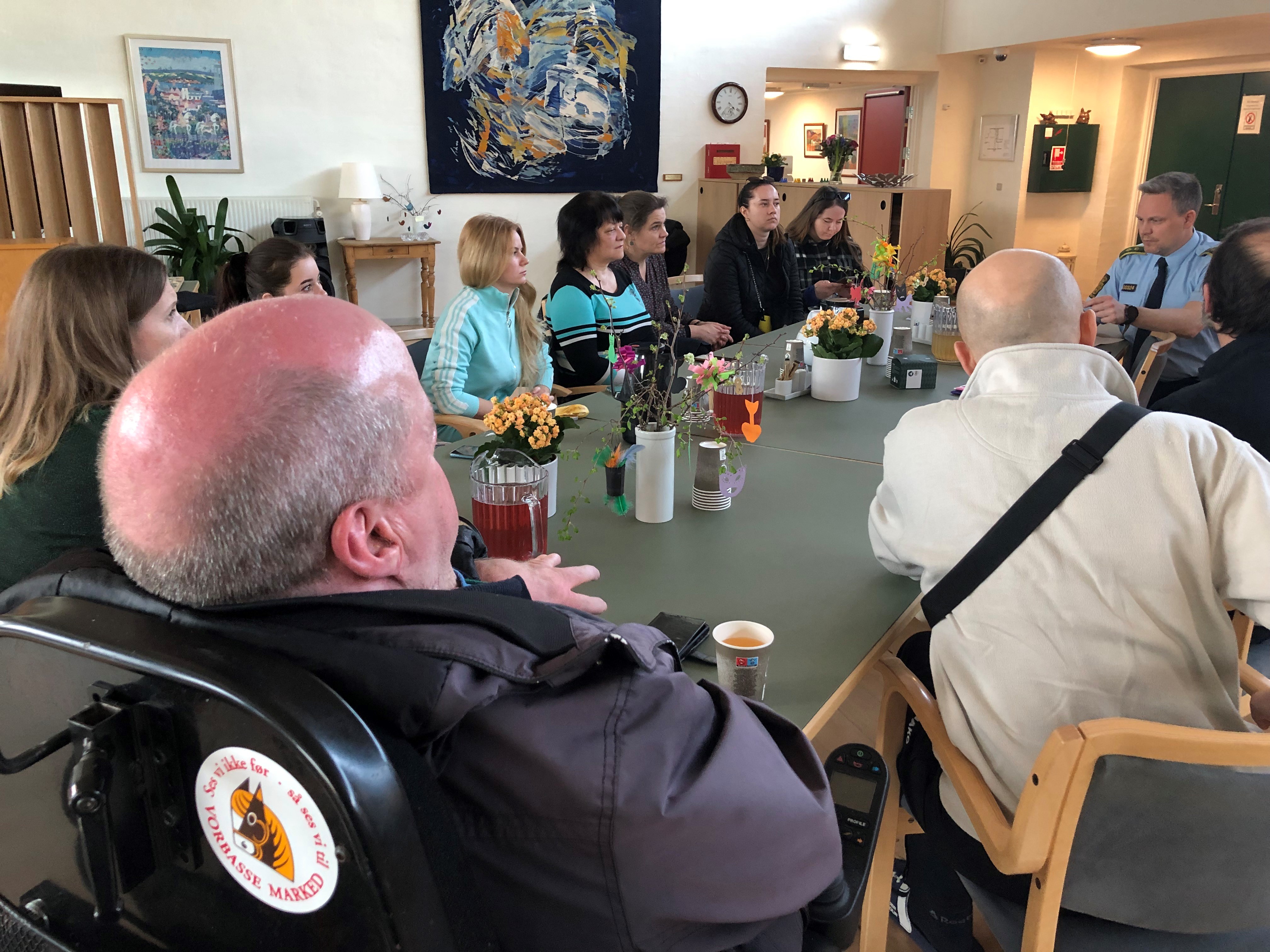 Mennesker der sidder omkring et bord og hører politibetjent fortælle om tryg digital kommune