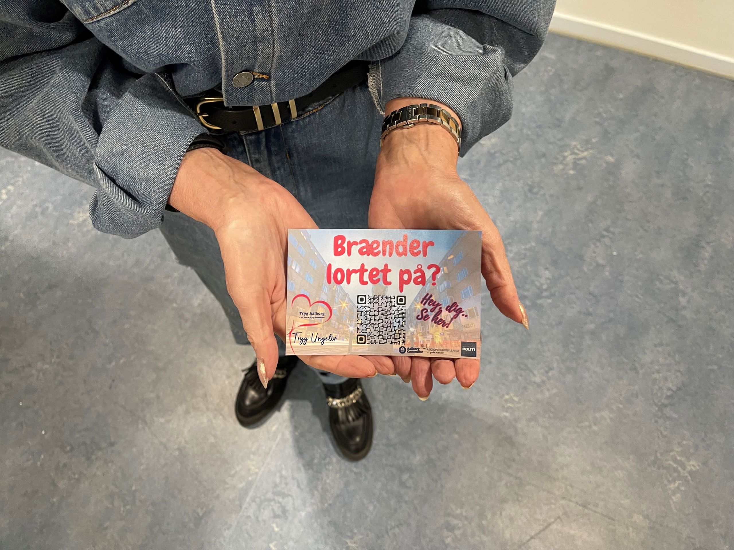 Uddeling af postkort med Brænder lortet på logo samt QR kode til hjemmesiden. Logoer fra Tryg Aalborg, Nordjyllands Politi og Aalborg Kommune.
