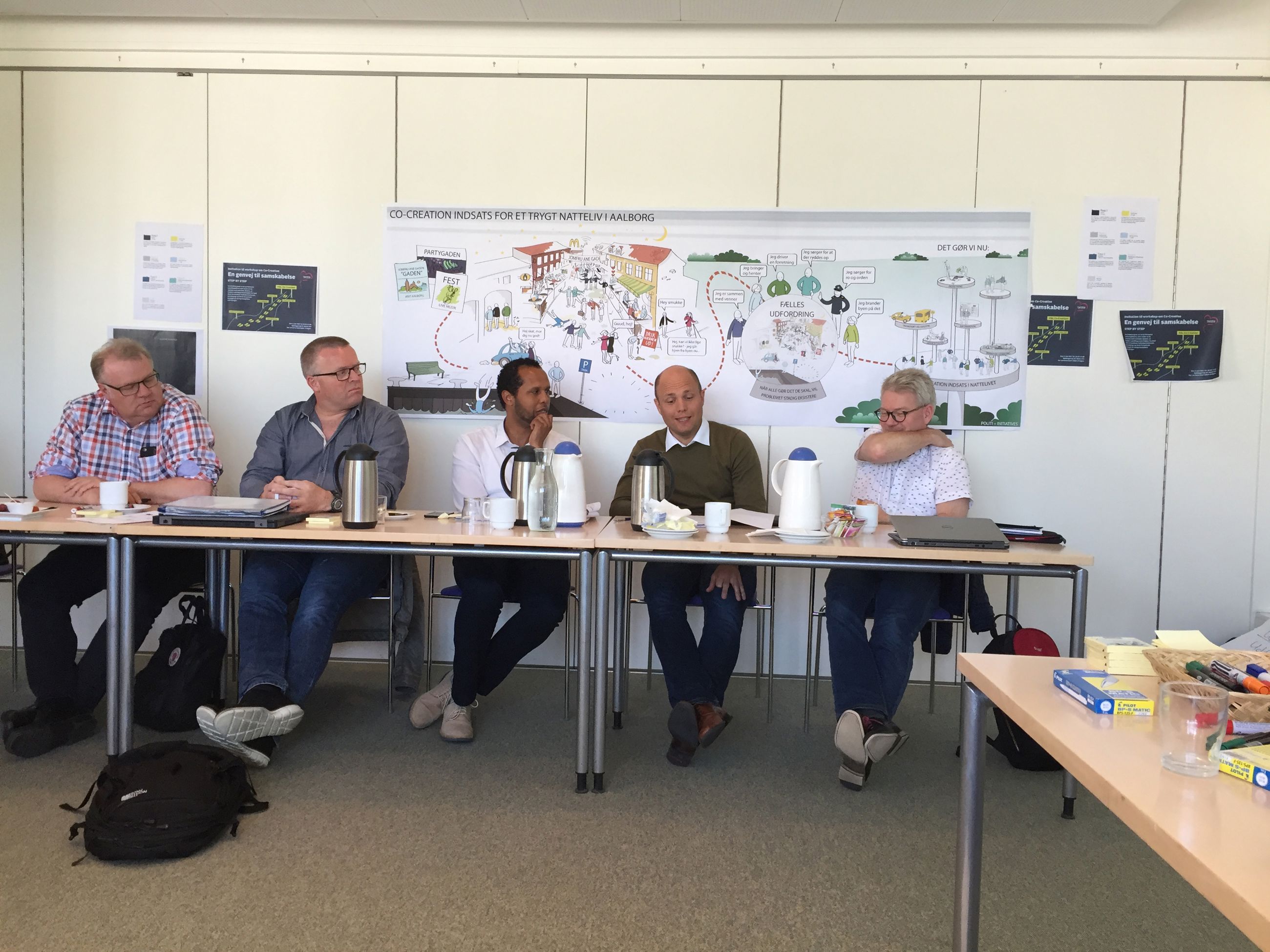 Fem mennesker, der sidder ved siden af hinanden ved et langt bord