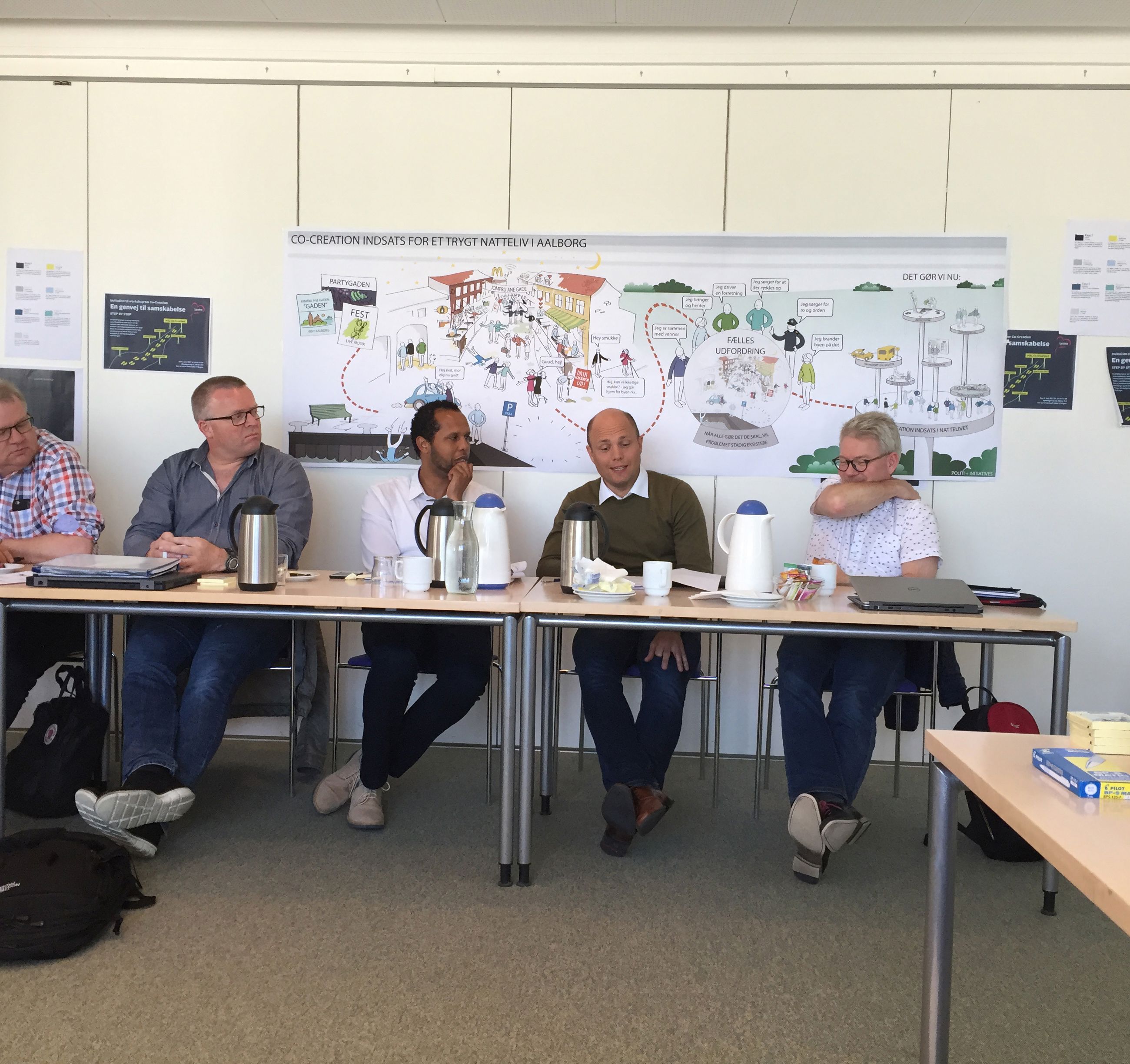 Fem mennesker, der sidder ved siden af hinanden ved et langt bord