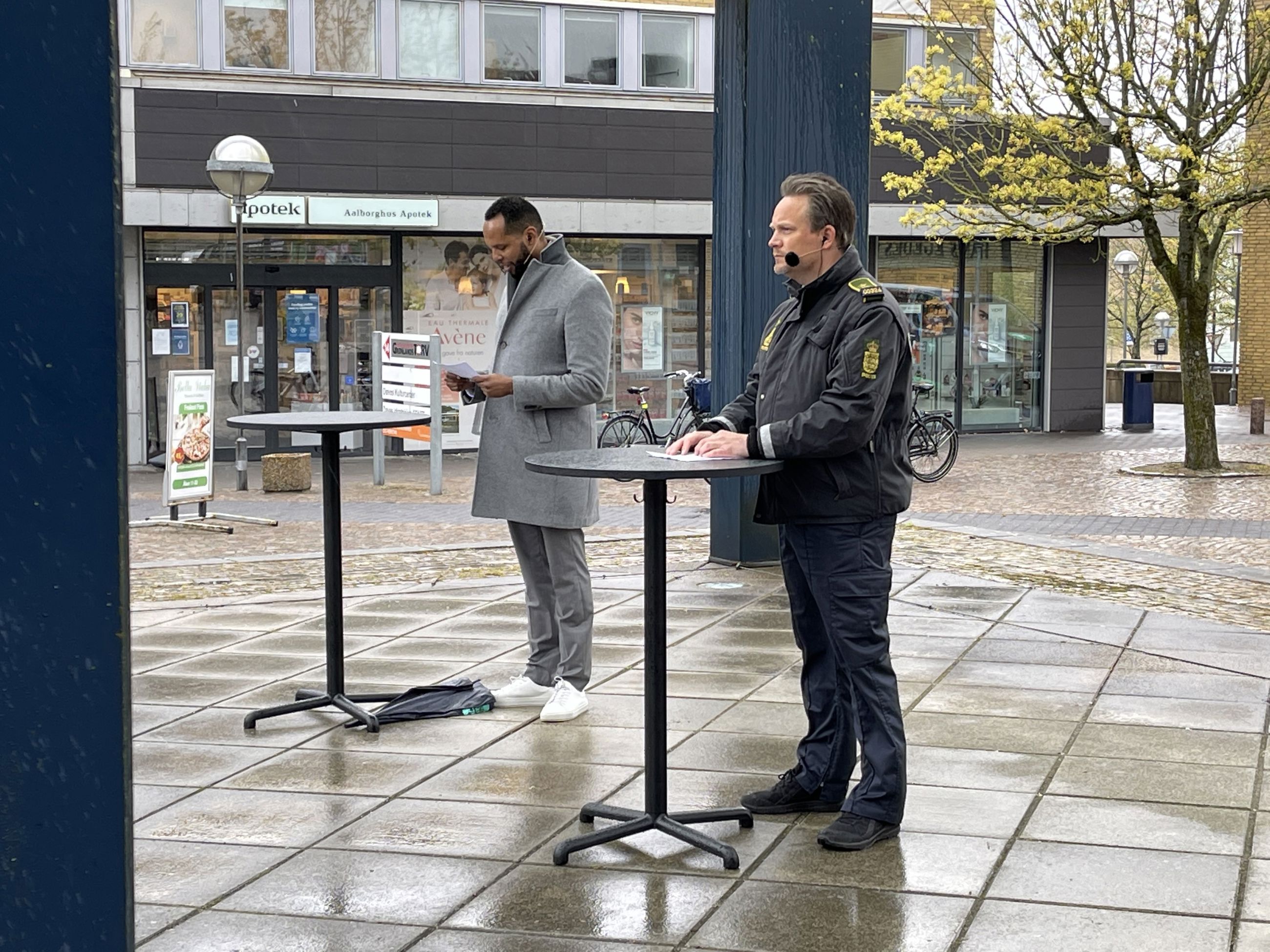 En politibetjent og en mand, der står ved borde, opstillet på gaden